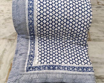 Könnte beinhalten: Aufgerollte blau-weiß gemusterte Steppdecke. Die Steppdecke hat ein sich wiederholendes geometrisches Design in Marineblau auf weißem Hintergrund. Der Rand hat ein Streifenmuster und florale Akzente. Die Steppdecke ist gefaltet und wirkt weich und bequem.