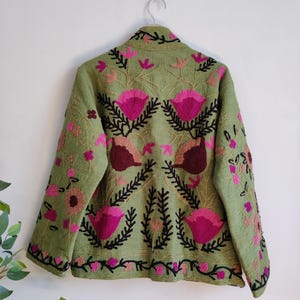 Puede incluir: Una chaqueta verde bordada con dise&ntilde;os florales rosas y negros. La chaqueta tiene un cuello alto y mangas largas.