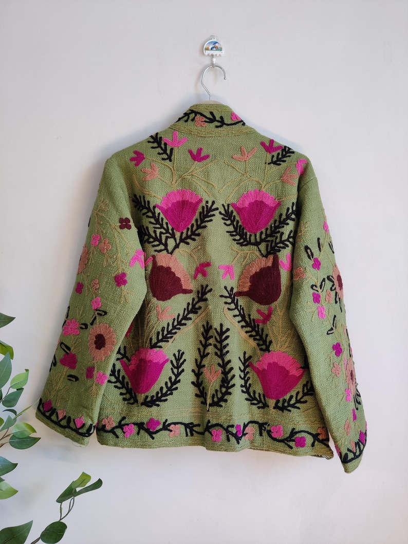 Puede incluir: Una chaqueta verde bordada con dise&ntilde;os florales rosas y negros. La chaqueta tiene un cuello alto y mangas largas.