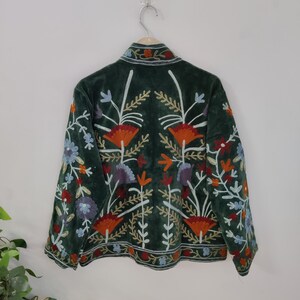 May include: A dark green jacket with colorful floral embroidery. The jacket features a velvet texture and a collar. The embroidery includes orange, blue, purple, and white flowers and leaves, creating a vibrant design.