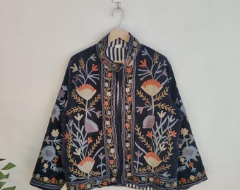 May include: A navy blue jacket with intricate floral embroidery in shades of orange, peach, blue, and purple. The jacket features a high collar with black and white stripes and is hanging on a wooden hanger.