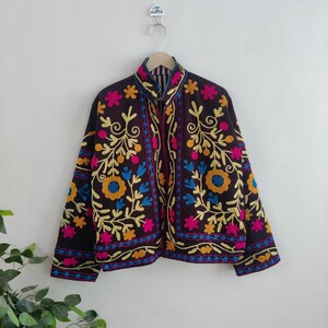 May include: A black jacket with colorful floral embroidery. The jacket features a high collar and is adorned with yellow, blue, and pink flowers and leaves. The embroidery is detailed and covers the front and sleeves of the jacket.