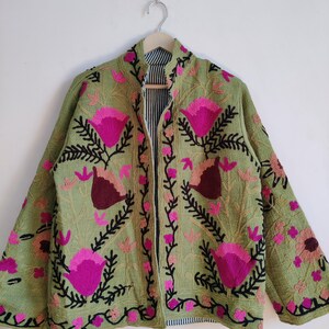 Puede incluir: Una chaqueta verde bordada con dise&ntilde;os florales rosas y marrones. La chaqueta tiene un cuello mandar&iacute;n y una cremallera frontal.