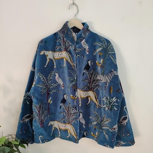Op de afbeelding: Blauw fluwelen jasje met een jungleprint met luipaarden, zebra's, toekans en palmbomen. De jas heeft een hoge kraag en lange mouwen, hangend aan een houten kleerhanger.