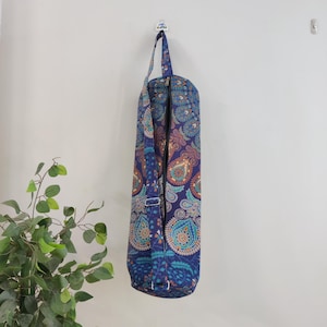 May include: A blue yoga mat bag with a colourful paisley pattern. The bag has a zipper closure and an adjustable shoulder strap.