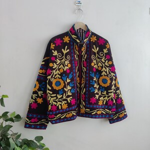 May include: A dark brown jacket with vibrant floral embroidery in yellow, pink, and blue. The jacket features a high collar and a full-length zipper. The floral design is intricately detailed, creating a bohemian aesthetic.