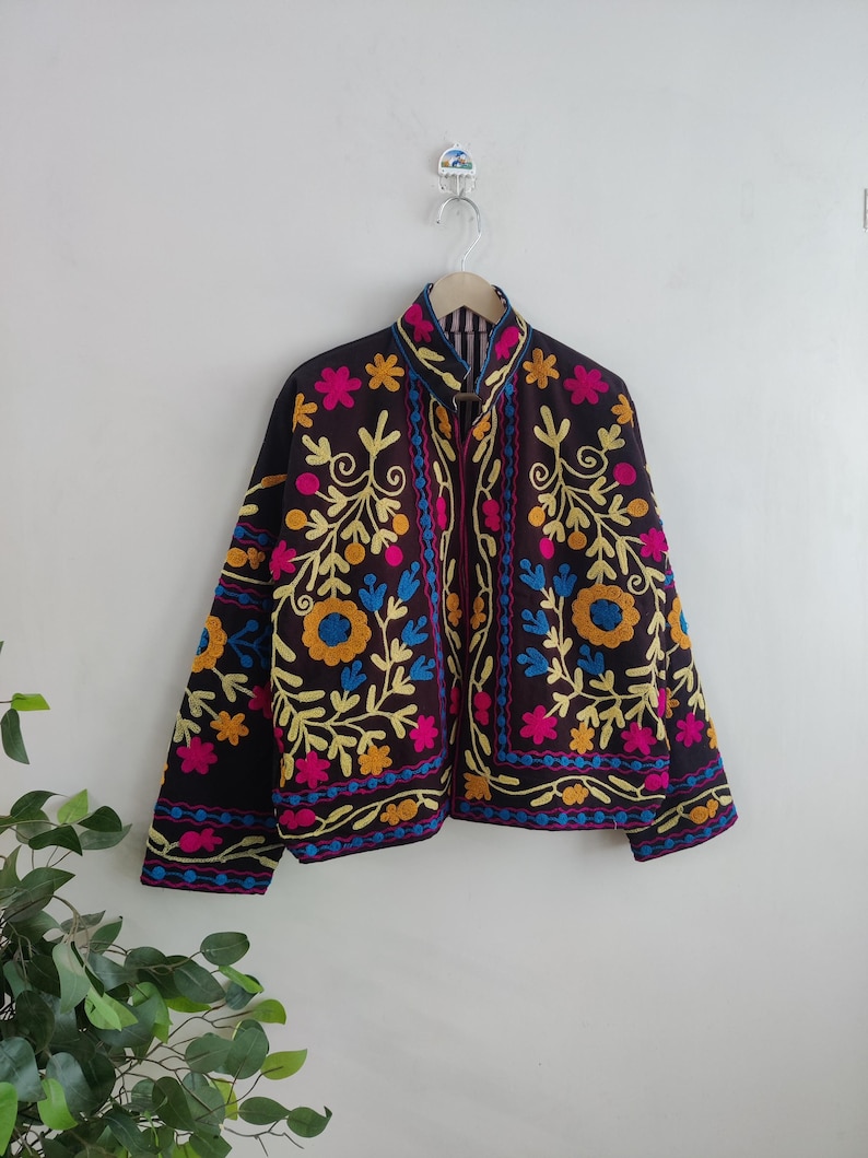 May include: A dark brown jacket with vibrant floral embroidery in yellow, pink, and blue. The jacket features a high collar and a full-length zipper. The floral design is intricately detailed, creating a bohemian aesthetic.