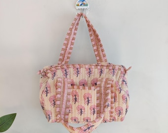 May include: A beige tote bag with a red and blue tree pattern and striped handles. The bag has a front pocket and a zipper closure. The bag is hanging on a white wall.