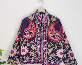 May include: A navy blue jacket with intricate embroidery in red, pink, and gold. The jacket features floral and paisley patterns, with a button-up front and a collar. The jacket is hanging on a wooden hanger against a white background.