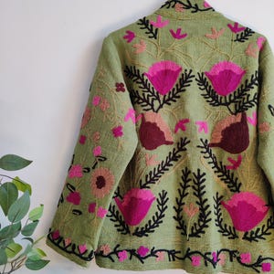 Puede incluir: Una chaqueta verde bordada con dise&ntilde;os florales rosas y marrones. La chaqueta tiene mangas largas y cuello.