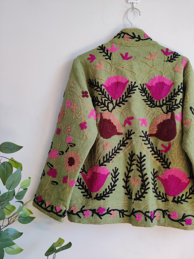 Puede incluir: Una chaqueta verde bordada con dise&ntilde;os florales rosas y marrones. La chaqueta tiene mangas largas y cuello.