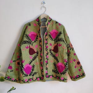 Puede incluir: Una chaqueta verde bordada con dise&ntilde;os florales rosas y negros. La chaqueta tiene un cuello mandar&iacute;n y mangas largas.