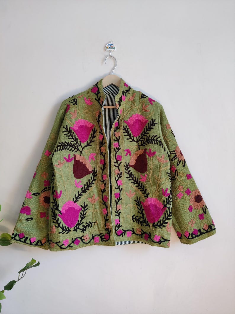 Puede incluir: Una chaqueta verde bordada con dise&ntilde;os florales rosas y negros. La chaqueta tiene un cuello mandar&iacute;n y mangas largas.