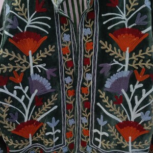 May include: A dark green velvet jacket with intricate floral embroidery in shades of orange, red, blue, and purple. The jacket features a mandarin collar and a striped lining, showcasing a bohemian style.