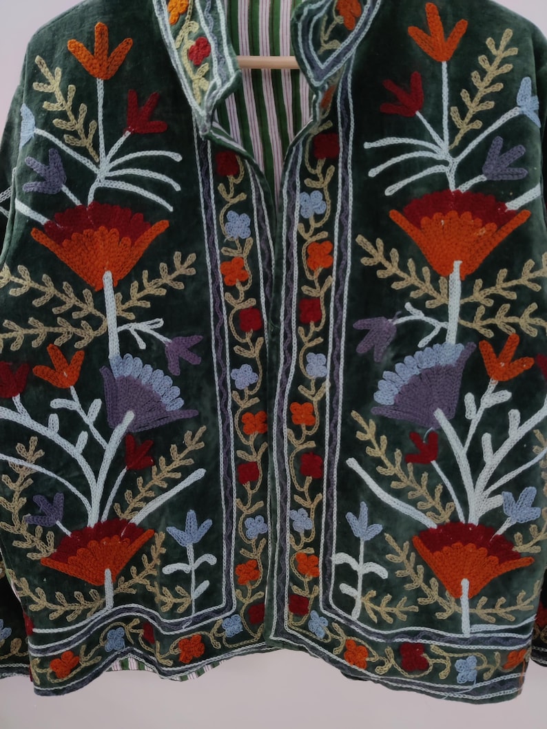 May include: A dark green velvet jacket with intricate floral embroidery in shades of orange, red, blue, and purple. The jacket features a mandarin collar and a striped lining, showcasing a bohemian style.