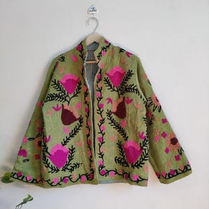Puede incluir: Una chaqueta verde bordada con dise&ntilde;os florales rosas y negros. La chaqueta tiene una cremallera y un cuello de pie.