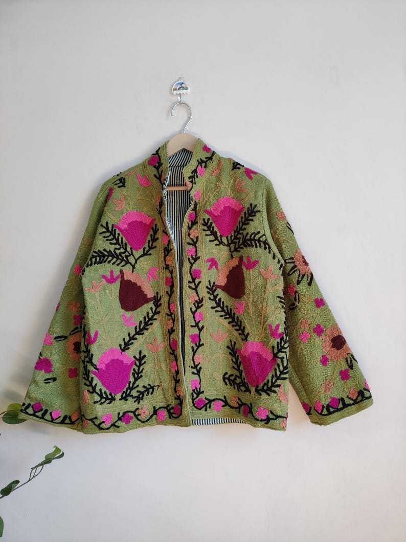 Puede incluir: Una chaqueta verde bordada con dise&ntilde;os florales rosas y negros. La chaqueta tiene una cremallera y un cuello de pie.
