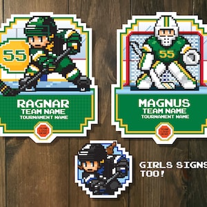 May include: Two pixel art hockey player signs with the names Ragnar and Magnus. The signs have a green and white color scheme. The signs have space for a team logo and tournament name. A smaller sign with a pixel art girl hockey player says "Girls Signs Too!"