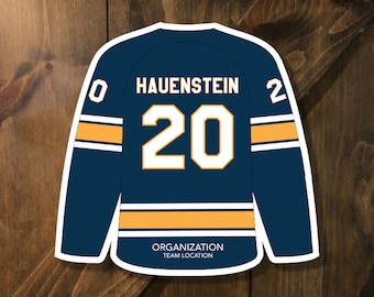 May include: A blue and gold hockey jersey with the number 20 and the name Hauenstein on the back. The jersey is on a wood background. The text below the jersey reads "Organization Team Location". The text below the jersey also reads "Final Cutout Size (8.5x11 paper): 7.5"w x 7.25"h (11x17 paper): 9.75"w x 9.325"h"