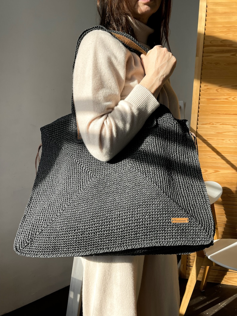 May include: A large black crocheted tote bag with leather straps and a brown leather tag that says "remarkable".