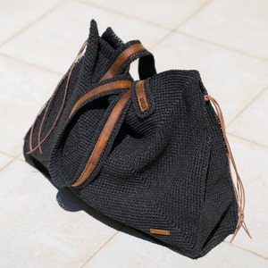 May include: A black crocheted tote bag with brown leather straps and a brown leather tag that says "Handmade".