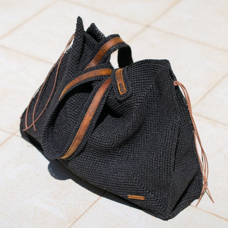 May include: A black crocheted tote bag with brown leather straps and a brown leather tag that says "Handmade".
