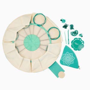 May include: A circular, cream-colored canvas case with a teal zippered pouch and a teal mandala design. The case opens to reveal a circular, teal-colored base with a metal frame holding 12 knitting needles. The case also includes a teal plastic needle gauge, a teal crochet hook, and a set of teal rubber bands.