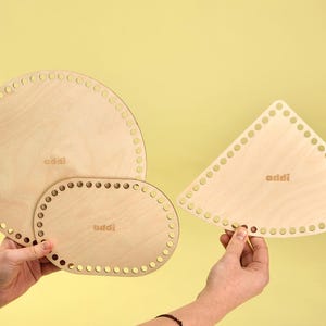 Op de afbeelding: Drie houten breinaalden in verschillende vormen en maten. De breinaalden zijn rond, ovaal en driehoekig. De breinaalden zijn gemaakt van lichtbruin hout en hebben gaten rond de randen. De breinaalden zijn in het midden gemarkeerd met "addi".