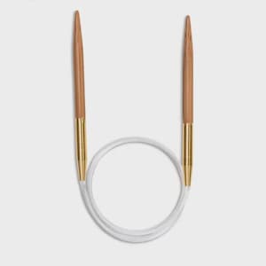 Pode incluir: Agulhas de tricô circulares com pontas de madeira castanho-claro e conectores de metal dourado. As agulhas são conectadas por um cabo branco e flexível, formando um círculo. Para projetos de tricô.