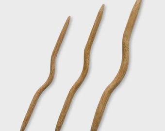 May include: Three wooden hair sticks with a curved, organic design. The sticks are made of light brown wood and have a smooth finish. The sticks vary in length, with the longest measuring approximately 7 inches.