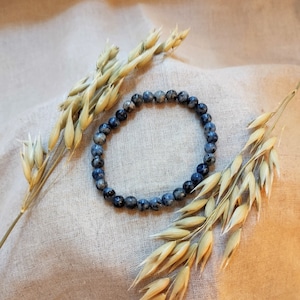 Op de afbeelding: Een blauwe en witte edelsteen armband met een natuurlijke, organische uitstraling. De armband is gemaakt van kleine, ronde kralen en ligt op een beige stoffen achtergrond.