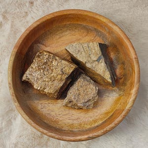 Peut inclure: Trois pierres brutes de couleur dorée dans un bol en bois. Les pierres ont un aspect naturel et non poli.