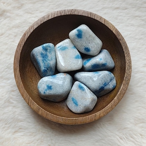 Peut inclure: Un bol en bois rempli de pierres de jaspe bleues et blanches roulées. Les pierres sont lisses et polies, avec une variété de motifs bleus et blancs.