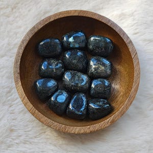 May include: A bowl of tumbled black obsidian stones. The stones are smooth and polished, with a dark, glassy sheen.