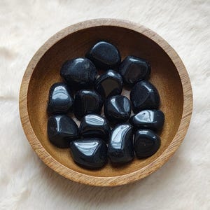 Peut inclure: Un bol de pierres d'obsidienne noire roulées. Les pierres sont lisses et polies, d'une couleur noire profonde.