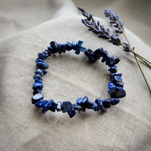 Peut inclure: Un bracelet en lapis-lazuli bleu avec un charme argenté. Le bracelet est composé de petites pierres de forme irrégulière.