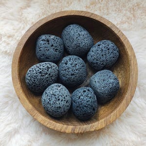 Peut inclure: Un bol contenant huit pierres de lave gris foncé. Les pierres sont lisses et ont une texture poreuse.