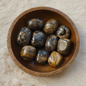 Peut inclure: Un bol en bois rempli de pierres roulées. Les pierres sont un mélange de noir et de brun avec des motifs tourbillonnants.