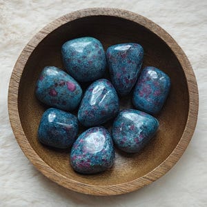 Peut inclure: Un bol en bois contenant huit pierres roulées bleues et roses. Les pierres sont lisses et ont un aspect moucheté.
