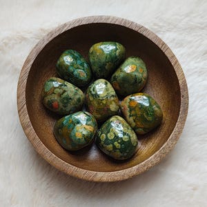 May include: A bowl of green, brown, and orange tumbled stones. The stones have a speckled pattern and are smooth and polished.