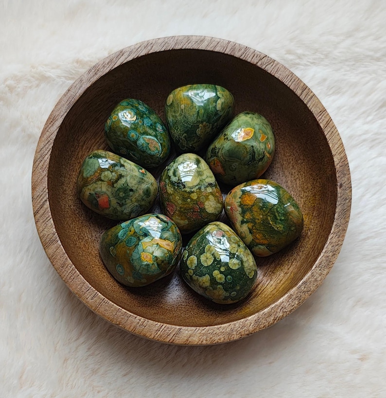 May include: A bowl of green, brown, and orange tumbled stones. The stones have a speckled pattern and are smooth and polished.