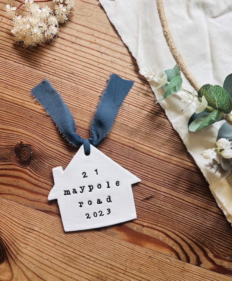 May include: White ceramic house ornament with the text "21 Maypole Road 2023" and a blue ribbon.