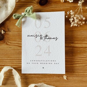 May include: A white card with the text "05 06 24" and "maise & thomas" in black script. The card also says "Congratulations on your wedding day" with a small heart symbol.