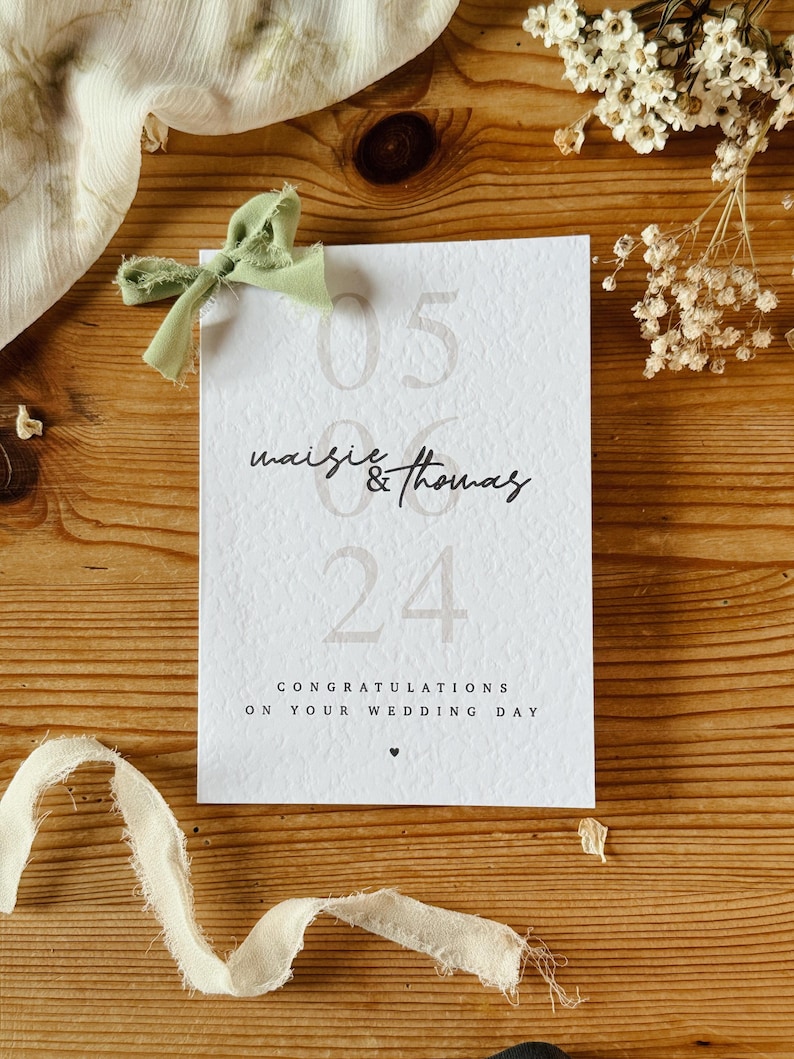 May include: A white card with the text "05 06 24" and "maise & thomas" in black script. The card also says "Congratulations on your wedding day" with a small heart symbol.