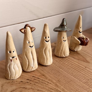 Peut inclure: Cinq petites figurines de fantômes en céramique en forme de cône avec un vernis beige clair. Chaque fantôme a un visage souriant peint à la main. L'un porte un chapeau marron, un autre un chapeau pointu vert foncé, un tient une citrouille.