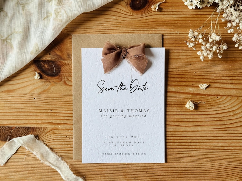May include: Save the Date card with a brown ribbon bow, featuring the text "Save the Date", "Maisie & Thomas are getting married", "5th June 2025", "Histlesham Hall Suffolk", and "formal invitation to follow".
