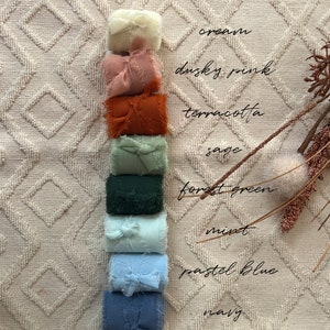 May include: A stack of fabric scraps in various colors, including cream, dusty pink, terracotta, sage, forest green, mint, pastel blue, and navy. The fabric scraps are arranged vertically on a white textured surface.