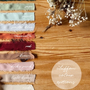 May include: A variety of chiffon fabric swatches in different colors, including navy, forest green, sage, mint, pastel blue, terracotta, red, brown, dusky pink, light brown, nude, and cream. The swatches are arranged vertically on a wooden surface. The text "chiffon colour options" is written in white on a circle in the lower right corner of the image.