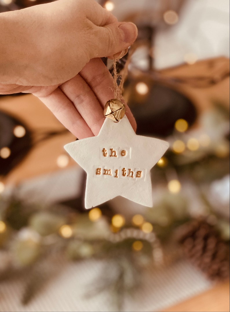 K&ouml;nnte beinhalten: Wei&szlig;er Keramik-Stern-Anh&auml;nger mit dem Text "the smiths" in goldenen Buchstaben. Der Anh&auml;nger hat eine goldene Glocke.