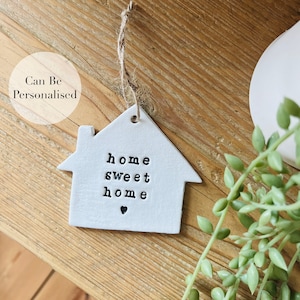 Może przedstawiać: Biała ceramiczna ozdoba w kształcie domu z napisem "home sweet home" i małym sercem. Ozdoba jest zawieszona na sznurku.